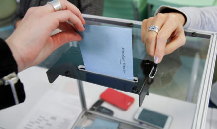 Main déposant une enveloppe dans une urne électorale